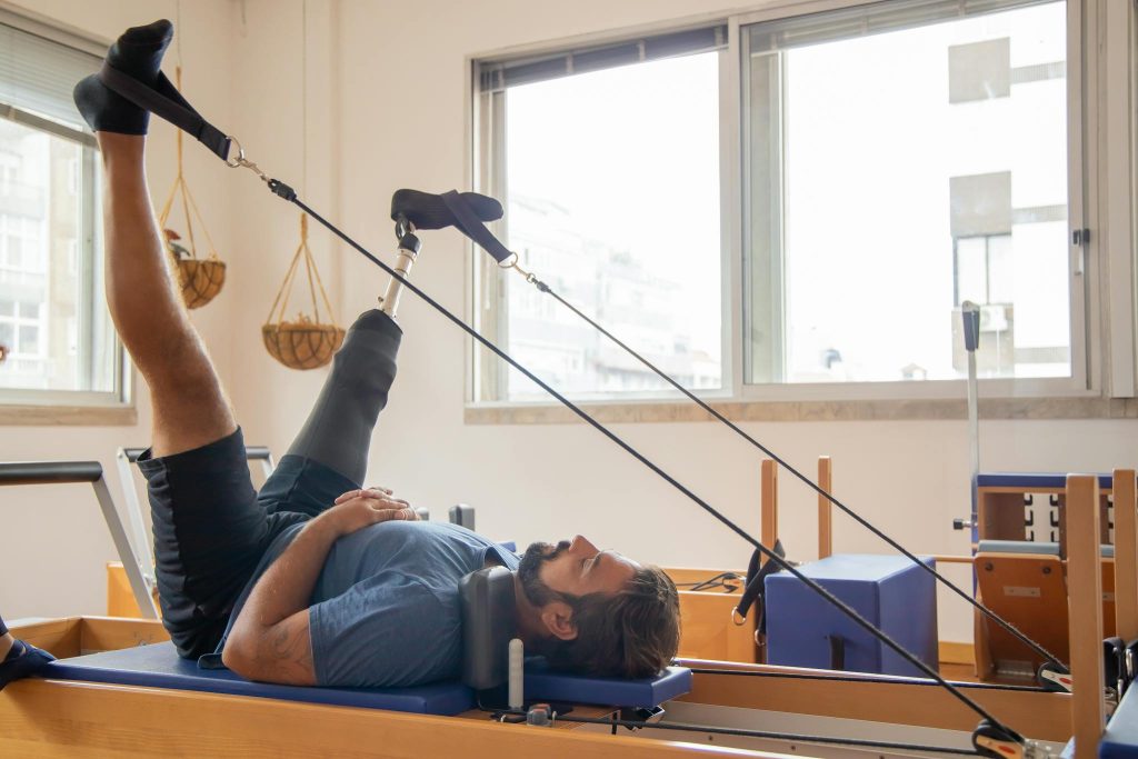 Man with prosthetic leg using pilates equipment for physical therapy indoors.